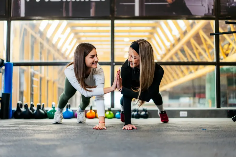 Two women performing a partner plank exercise in a gym