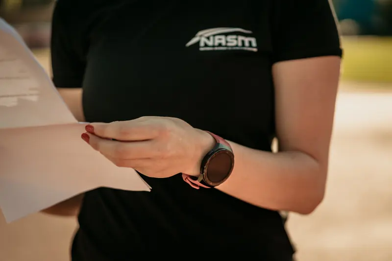 NASM-branded instructor holding assessment notes during a training session